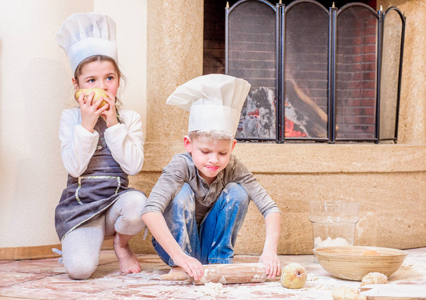 Zwei Geschwister - Junge und Mädchen - in Kochmützen am Kamin  - Foto, Bild