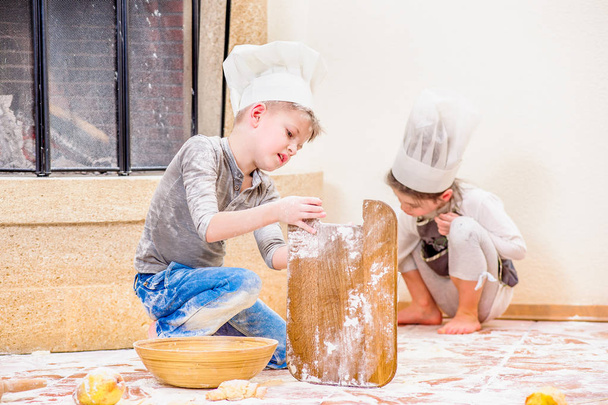 Dois irmãos - menino e menina - em chapéus de chef perto da lareira
  - Foto, Imagem