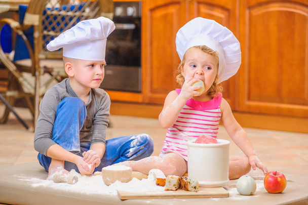 Two siblings - boy and girl - in chef 's hats sitting on the kitc
 - Фото, изображение