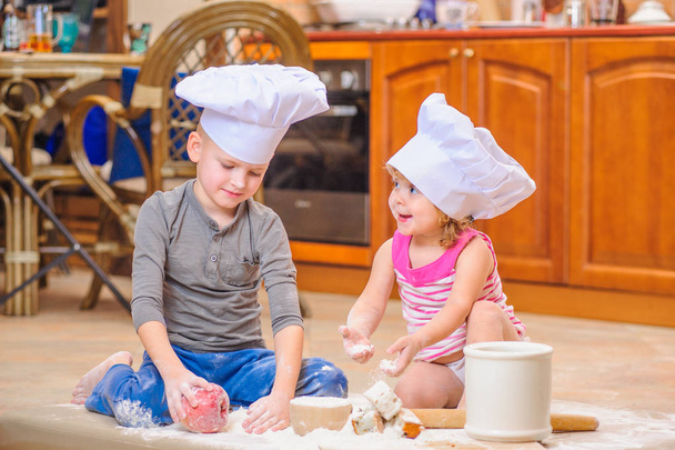 Two siblings - boy and girl - in chef's hats sitting on the kitc - Valokuva, kuva