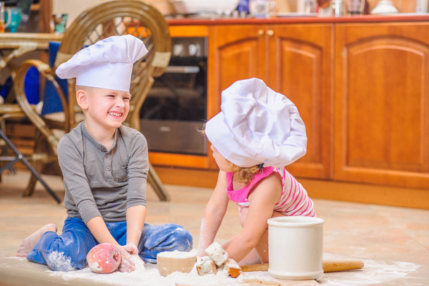 Dos hermanos - niño y niña - en sombreros de chef sentados en el kitc
 - Foto, Imagen
