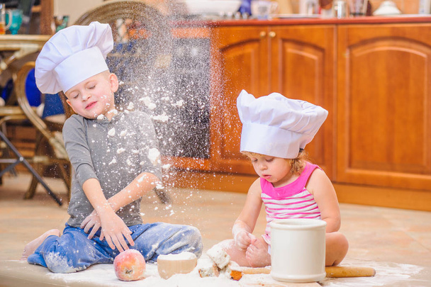 Two siblings - boy and girl - in chef's hats sitting on the kitc - Photo, Image