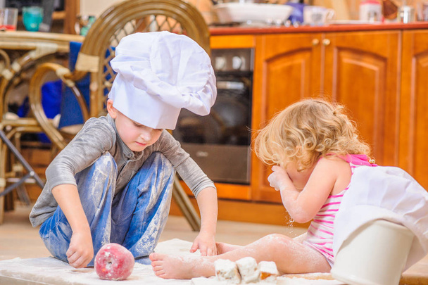 Two siblings - boy and girl - in chef 's hats sitting on the kitc
 - Фото, изображение