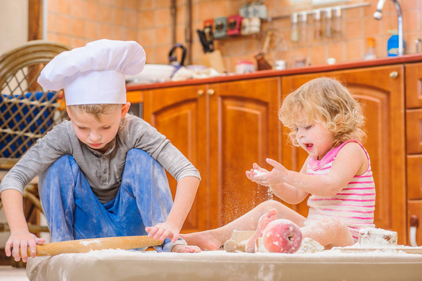 zwei Geschwister - Junge und Mädchen - in Kochmützen auf dem Kitsch sitzend - Foto, Bild