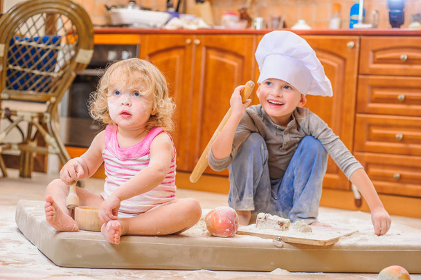 Dois irmãos - menino e menina - em chapéus de chef sentados no kitc
 - Foto, Imagem