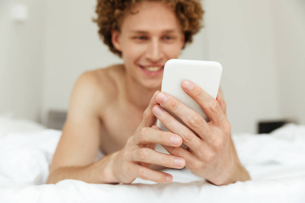Cheerful handsome man lies in bed chatting by phone - Photo, image