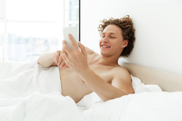 Smiling attractive man with curly hair using mobile phone - Foto, imagen
