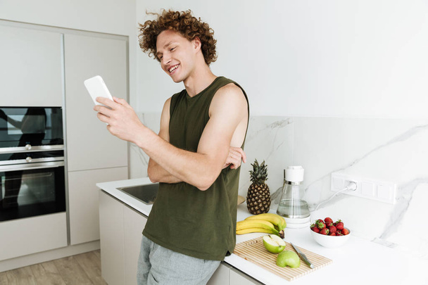 Man standing at the kitchen and chatting by phone - Foto, afbeelding