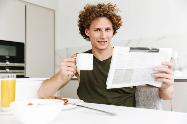 Man sitting at the kitchen while holding newspaper - Фото, изображение