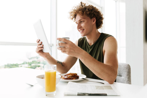 Handsome happy man using tablet computer and drinking coffee - Photo, image