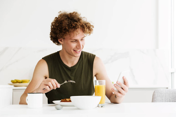Cheerful man using mobile phone and eating pastries - Photo, Image