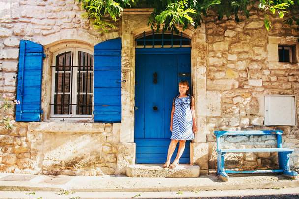 Pretty little girl tourist on the streets of Provence, Wearing blue gingham dress, sunglasses and backpack. Travel with children concept. Image taken in Arles, France - Foto, Bild