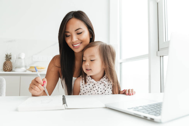 Mom with little cute asian girl using laptop writing notes - Fotoğraf, Görsel