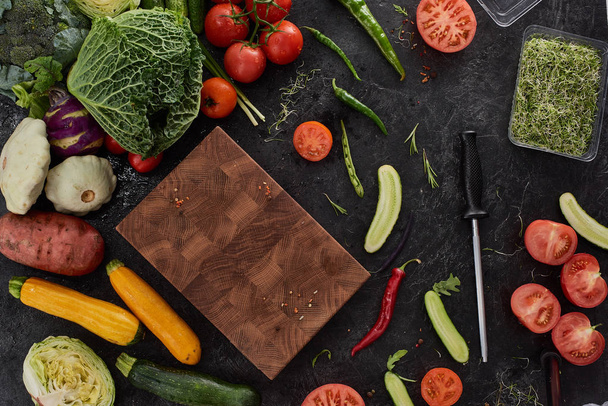 Taze organik yeşil soğan sebze kesme tahtası üzerinde siyah taş Resepsiyon arka plan üzerinde. Sağlıklı doğal gıda rustik ahşap üzerine. Domates, marul, havuç, biber, kabak ve diğer malzemeler üstten görünüm pişirme - Fotoğraf, Görsel