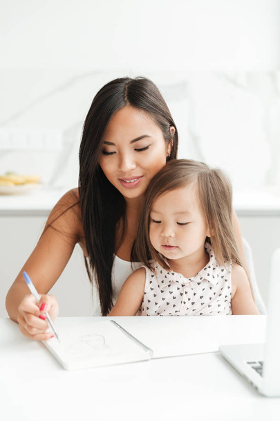 Mom with little cute asian girl using laptop writing notes - Foto, imagen