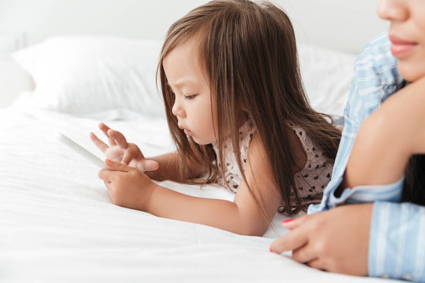 Babymeisje spelen met smartphone terwijl liggend in bed - Foto, afbeelding