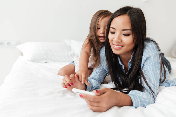 Amazing young woman with little daughter using mobile phone. - 写真・画像