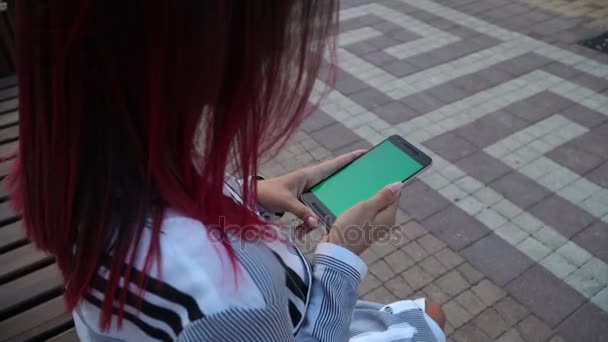 Girl in dress seated in park and use smart phone CHROMA KEY screen - Πλάνα, βίντεο