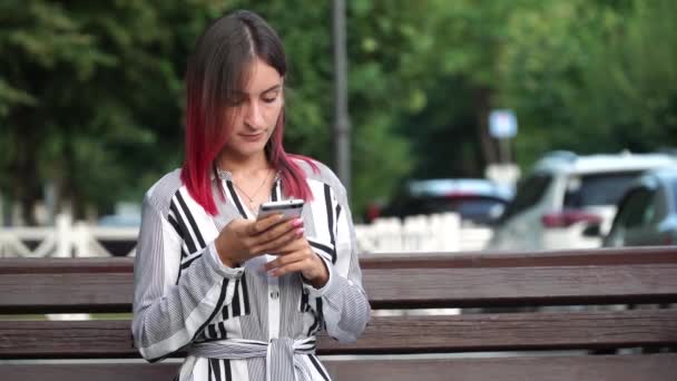 Pretty girl using smartphone in city park, pinc hair - Materiał filmowy, wideo