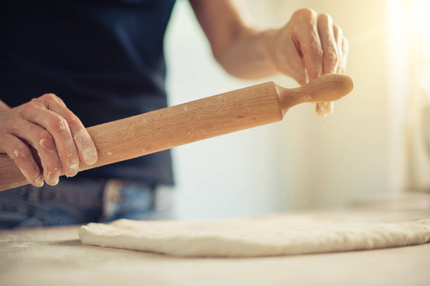 Woman rolling dough on wooden table with wooden rolling pin - Zdjęcie, obraz