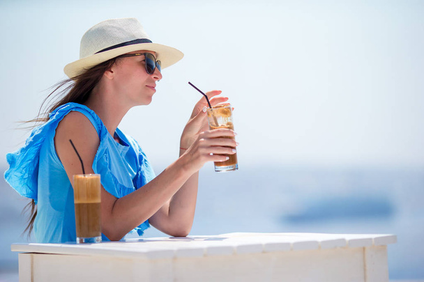 Young girl drinking cold coffee enjoying sea view. Beautiful woman relax during exotic vacation on the beach enjoying frappe - Foto, Bild