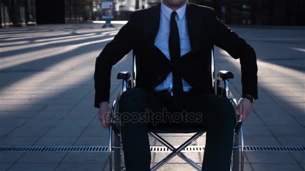 Калека бизнесмен переезжает в инвалидной коляске на камеру на открытом воздухе рядом с бизнес-центром
. - Кадры, видео