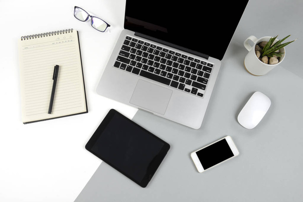 Office table with laptop computer, notebook, digital tablet and mobile phone on modern two tone (white and grey) background. - 写真・画像