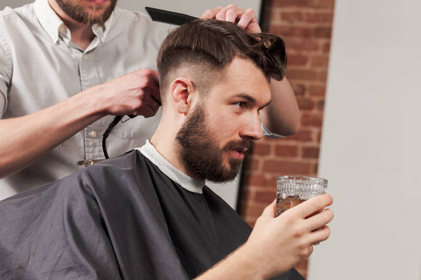 Young handsome barber making haircut of attractive man in barbershop - Foto, Imagem
