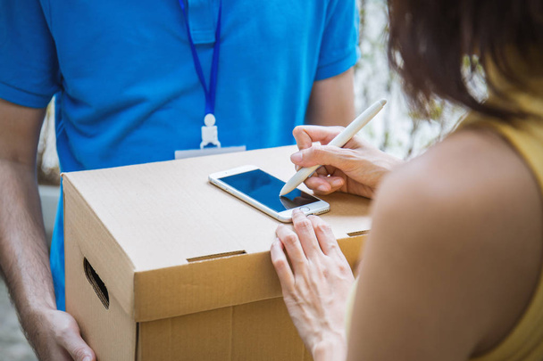 Woman appending sign signature after accepting receive a delivery of boxes from deliveryman, receive and delivery concept  - 写真・画像