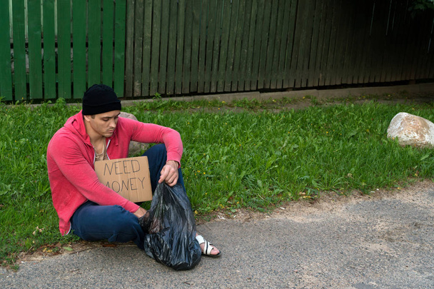 Un SDF assis sur le trottoir avec un carton et une inscription : besoin d'argent
 - Photo, image
