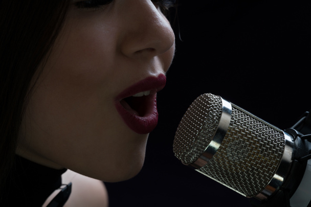 Singer in front of a microphone. Isolated on a dark background - Photo, Image