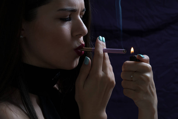 Портрет красивой элегантной девушки, курящей сигарету на тёмном фоне
 - Фото, изображение