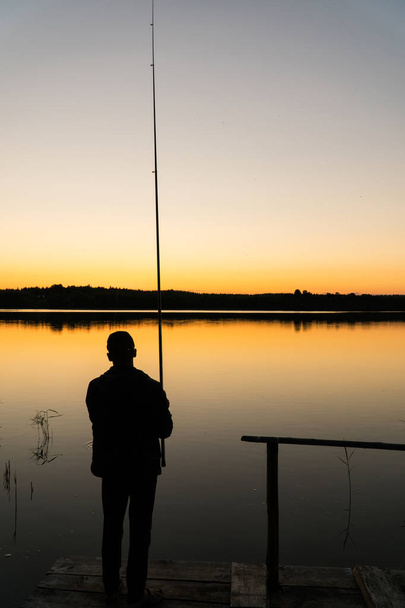 Siluettikalastaja auringonlaskun aikaan. Mies kalastelee laiturilla auringonlaskun aikaan.
 - Valokuva, kuva