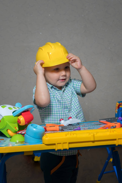 A child in a construction helmet with toy tools repairs toys - Photo, Image