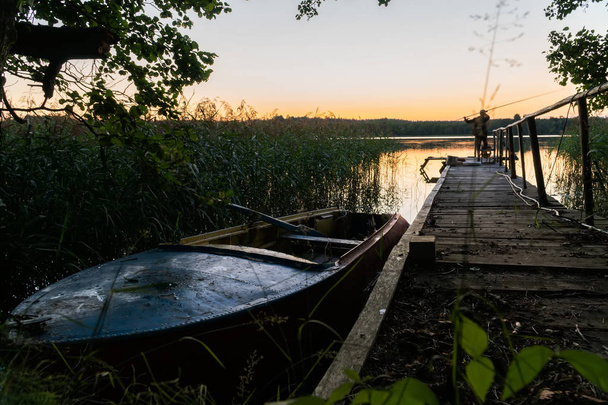 O velho barco no cais ao pôr-do-sol. À distância pode-se ver a silhueta de um pescador
 - Foto, Imagem