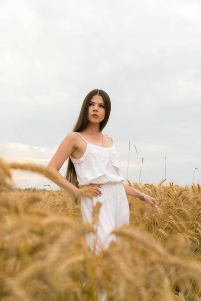 A girl in a white summer suit is standing in a field of wheat - Foto, afbeelding