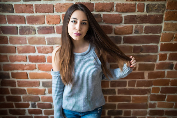 Beautiful young woman in casual wear smiling, standing against white brick wall - Photo, Image