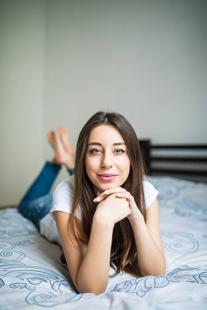 Genç kadın, gülümseyerek başını eliyle saçlarını diğerinde üzerine istirahat yatağın ucundaki yalan. - Fotoğraf, Görsel