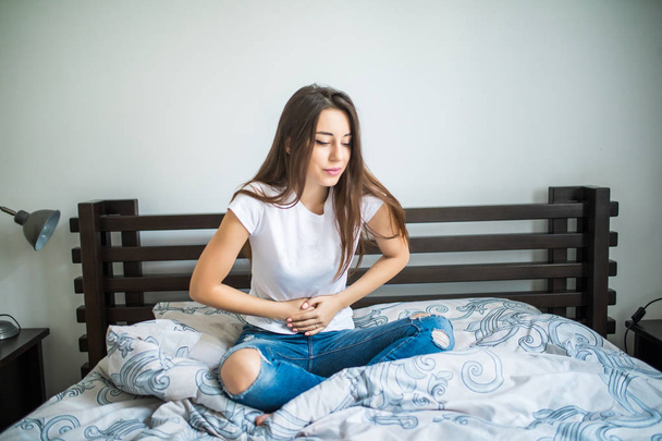 Młoda piękna kobieta cierpi na ból brzucha siedząc na łóżku w domu - Zdjęcie, obraz