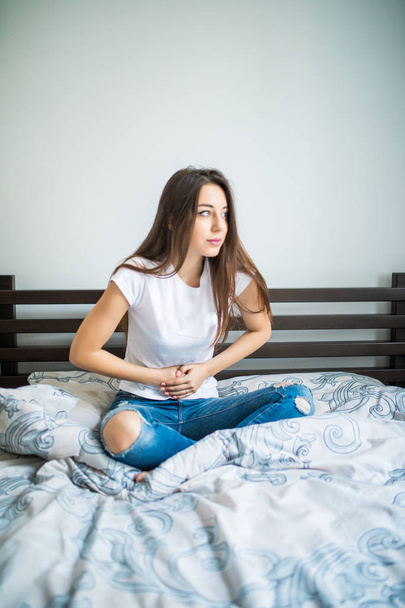 Young beauty woman suffering from abdominal pain while sitting on bed at home - Foto, Imagen