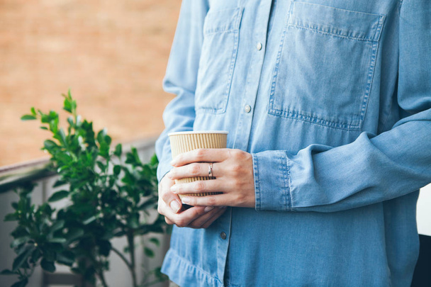 青のカジュアルなジーンズ シャツの若い女性がコーヒーを飲む.  - 写真・画像