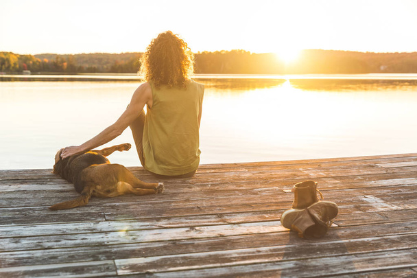 Woman and dog relaxing on the dock at sunset - Photo, image