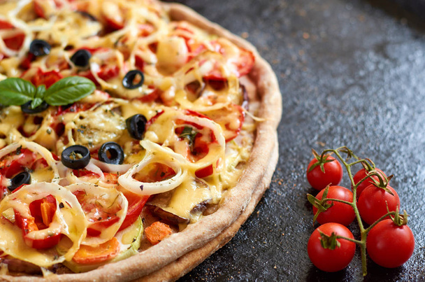 Meleg vegetáriánus pizza paradicsom, paprika, hagyma, fekete olívabogyó, sajt és fűszerek, fekete, sötét háttér közelről díszített friss bazsalikomos koktélparadicsommal - Fotó, kép