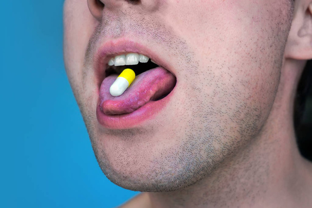 Primer plano de una píldora blanca en la boca del hombre
. - Foto, Imagen