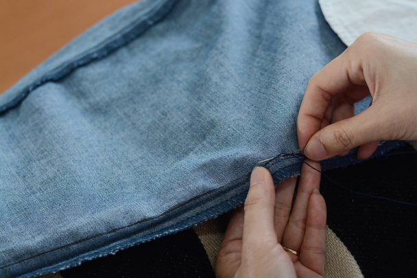 Handmatige naaien moment door handen: invoegen van de naald in de stof - Foto, afbeelding