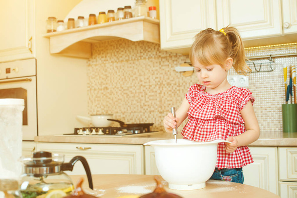 Ładna mała dziewczynka pomocnika pomaga jej matka, gotowanie w kuchni. Szczęśliwy, kochający rodziny przygotowują piekarnia. - Zdjęcie, obraz