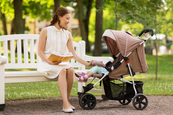 mother with child in stroller reading book at park - Fotoğraf, Görsel