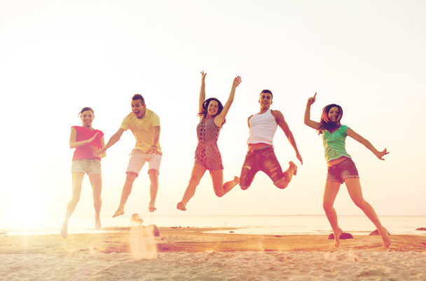 smiling friends dancing and jumping on beach - Foto, Imagen