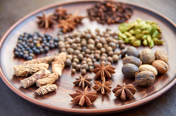 Aromatic spices on a dark plate - star anise, fragrant pepper, calamus root, cinnamon, nutmeg close up on brown background. Spices texture background - Photo, Image