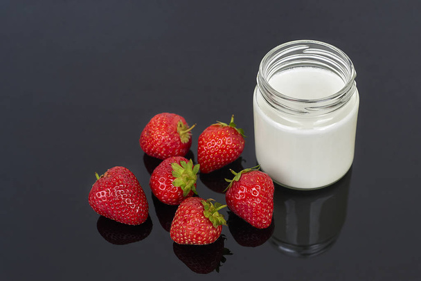 Glass jar with yogurt and six strawberries on a black background horizontal - Photo, Image